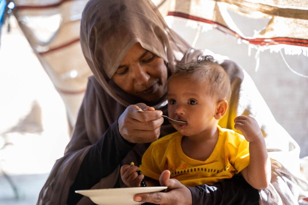 Am 22. Februar 2023 hält Sabna Mohamed ihre 9 Monate alte Tochter Fatuma auf dem Schoß, während sie sie in ihrem Haus im Dorf Wager im Norddelta im Bundesstaat Kassala im Sudan mit Linsen füttert.