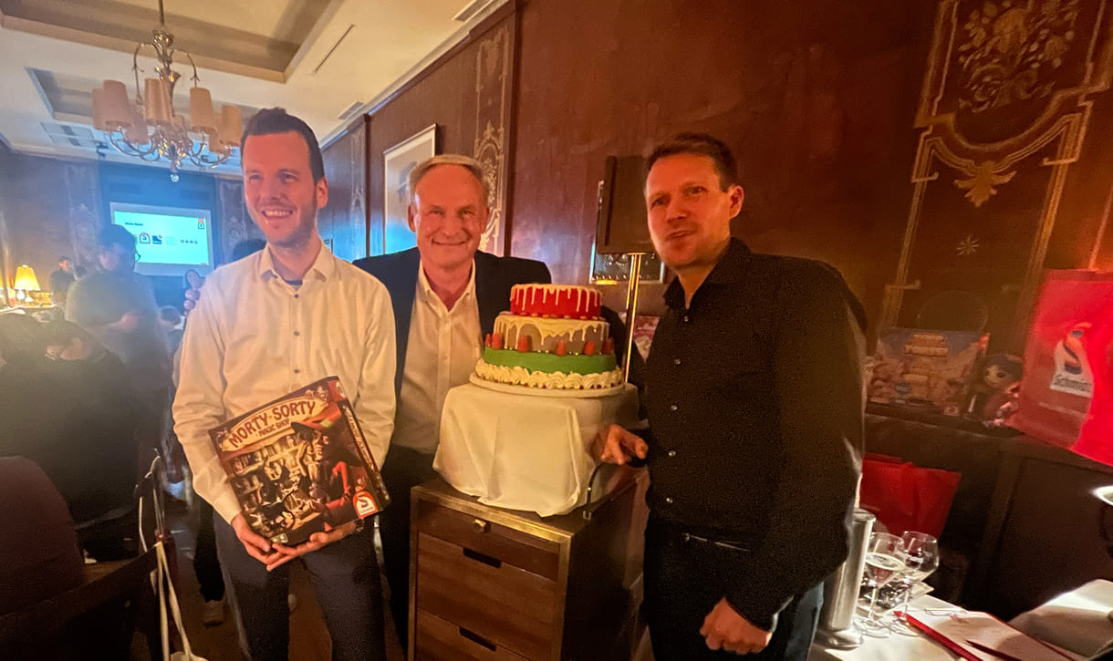 Echte Torte als süße Zusatz-Auszeichnung für das preisgekrönte Brettspiel - mit Erfinder Wolfgang Warsch (rechts) und Schmidt-Spiele-Geschäftsführer Axel Kaldenhoven sowie „Morty Sorty Magic Shop“-Erfinder Markus Slawitscheck (links)
