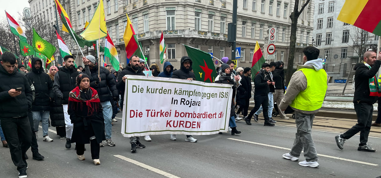 Auf diesem Transparnt wird auf den Kampf von Kurd:innen gegen ISIS, den sogenannten Islamischen Staat hingewiesen - und die Bombardierung Rojavas durch türkisches Militär