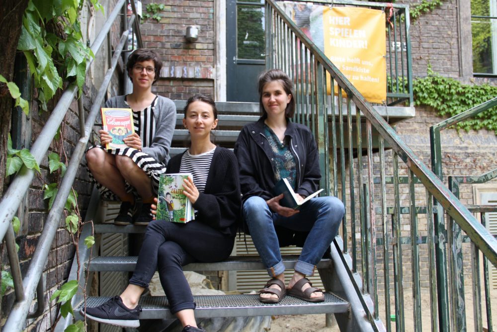 Drei junge Frauen mit Büchern sitzen auf einer Metall-Stiege im WuK-Hof: Greta Egle, Kathi Pech und Sara Schausberger