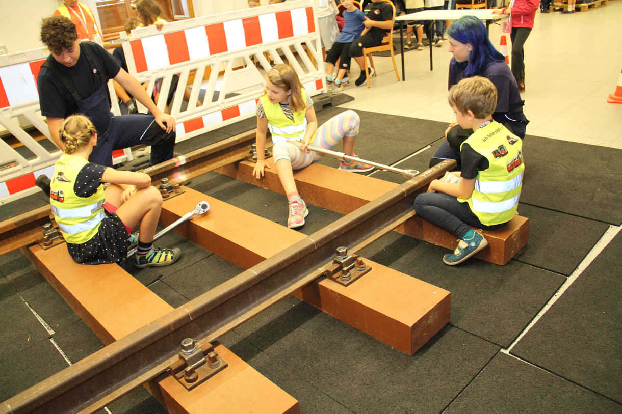 Kinder lösen Muttern udn Schrauben eines U-Bahngleises und fixieren sie anschließend wieder