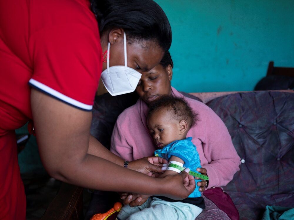 In Lusikisiki Ngobozana (Südafrika) überprüft eine Pflegekraft Marlons Genesung von akuter Unterernährung, während seine Mutter Nomakhosazandas Kind hält