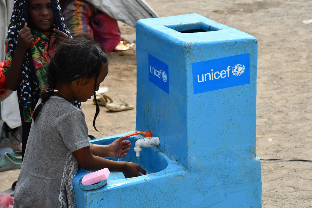 Ein junges Mädchen wäscht sich die Hände, bevor es den kinderfreundlichen, sicheren Lernraum Abnaa Al-Shamal in Port Sudan betritt. Dort haben täglich mehr als 100 Kinder Zugang zu integrierten Diensten wie Spielen, Zeichnen, Singen, Spielen, psychosozialer Unterstützung, die für ihr geistiges Wohlbefinden entscheidend ist, digitalem Lernen, Wasser, Sanitäranlagen und Hygiene sowie Gesundheitsversorgung.