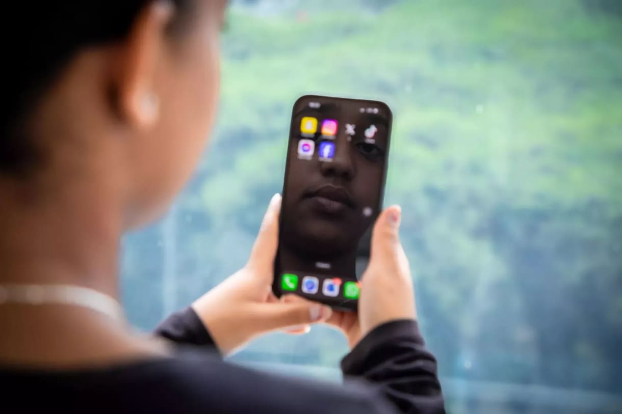 Jugendliche mit Smartphone und eingien erkennbaren Social-Media-App-Icons sowie einem Gesicht - vlt. als Screen-Hintergrund oder aus einem Video-Telefonat