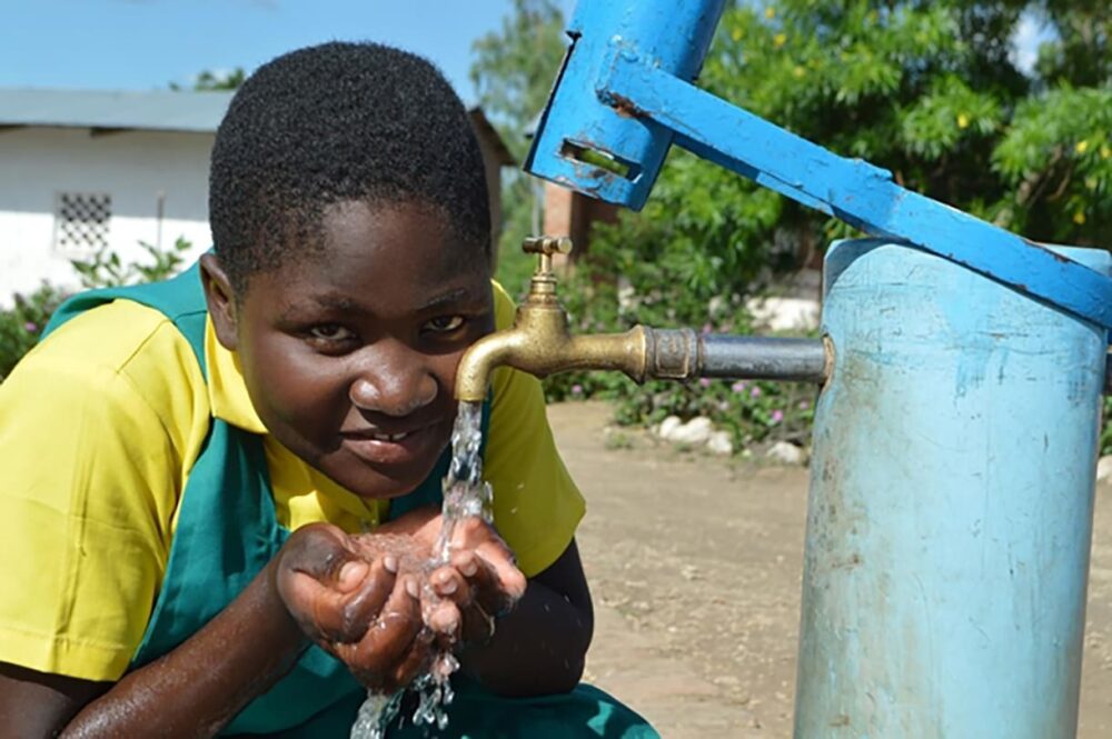 Charity Kalibwanji trinkt Wasser aus einem von UNICEF installierten solarbetriebenen Bohrloch an ihrer Schule.