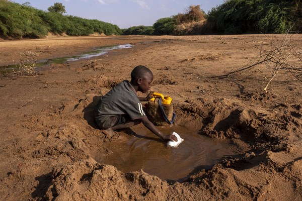 Ein kleiner Junge sammelt das wenige Wasser, das er aus einem wegen der großen Dürre ausgetrockneten Fluss holen kann, in Somalia