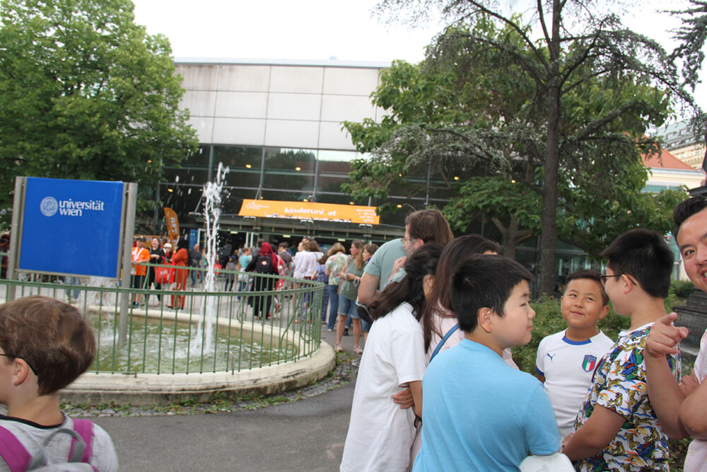 Lange Schlangen von Kinderuni-Studierenden und ihren erwachsenen Begleitpersonen beim Abholen der Studien-Ausweise und Jubiläums-T-Shirts